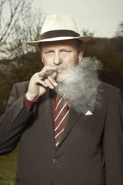 Bad evil man in mob style smoking cigar outdoor - 写真・画像