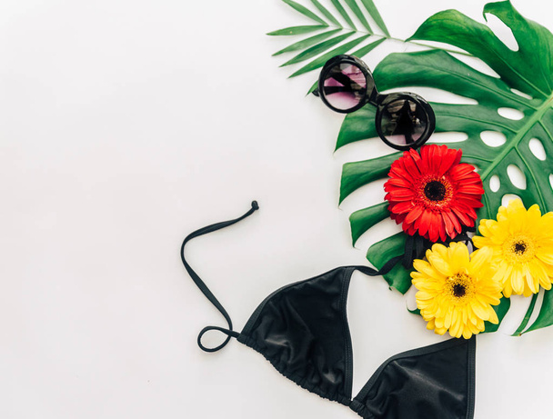 Summer concept. Sunglasses and bikini over tropical leaf monstera with flowers. Flat lay  - Fotó, kép