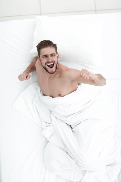 top view. happy man sitting on the comfortable bed - Fotoğraf, Görsel