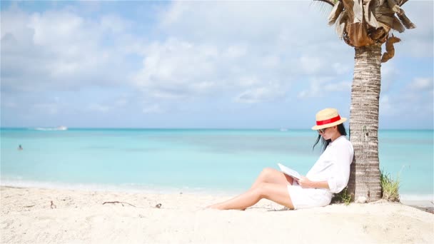 Молодая женщина читает книгу во время тропического белого пляжа - Кадры, видео