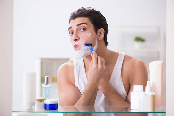 Молодой красивый мужчина бреется рано утром дома - Фото, изображение