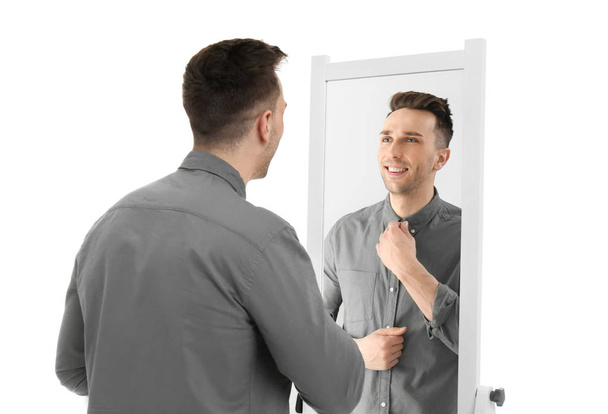 Young man looking at himself in mirror on white background - Φωτογραφία, εικόνα