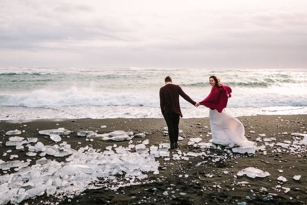 Wedding Couple is walking together on Black Sand Beach, Iceland. Artwork - Foto, afbeelding
