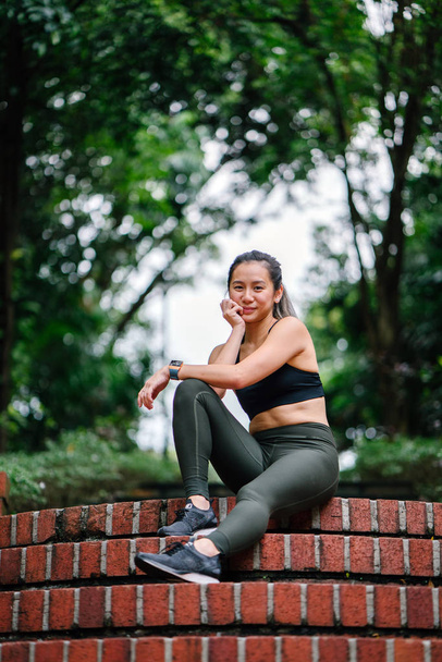 Portrait of an attractive, young Chinese Asian woman dressed in sporty, active wear on a bridge in a lush, green public park in Singapore during the day on the weekend. - Fotografie, Obrázek