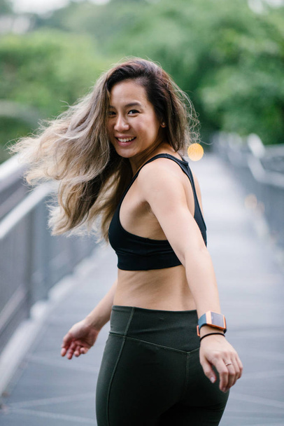 Portrait of an attractive, young Chinese Asian woman dressed in sporty, active wear on a bridge in a lush, green public park in Singapore during the day on the weekend. - Foto, immagini