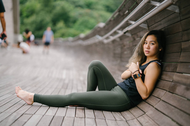 Portrait of an attractive, young Chinese Asian woman dressed in sporty, active wear on a bridge in a lush, green public park in Singapore during the day on the weekend. - Foto, Bild