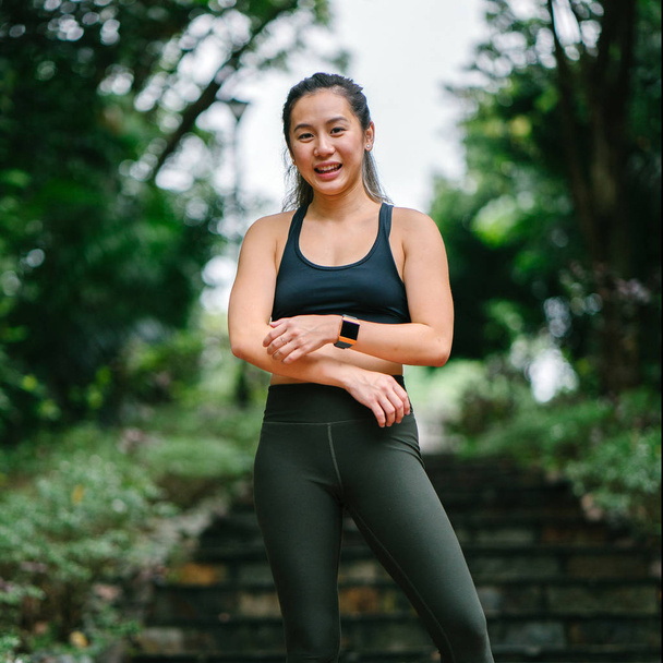 Portrait of an attractive, young Chinese Asian woman dressed in sporty, active wear on a bridge in a lush, green public park in Singapore during the day on the weekend. - Фото, зображення