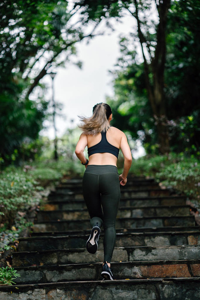 attractive, young Chinese Asian woman dressed in sporty, active wear running down stairs on a path in a public park in Singapore during her weekend workout. - Фото, зображення