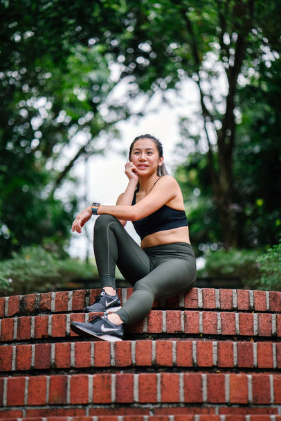 Portrait of an attractive, young Chinese Asian woman dressed in sporty, active wear on a bridge in a lush, green public park in Singapore during the day on the weekend. - Foto, Imagem