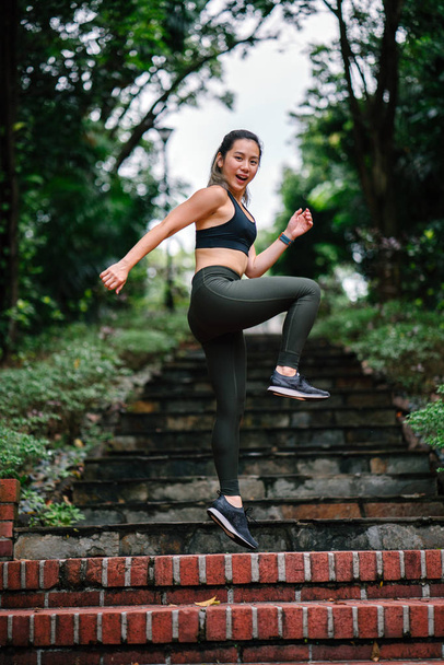 attractive, young Chinese Asian woman dressed in sporty, active wear running down stairs on a path in a public park in Singapore during her weekend workout. - Foto, afbeelding
