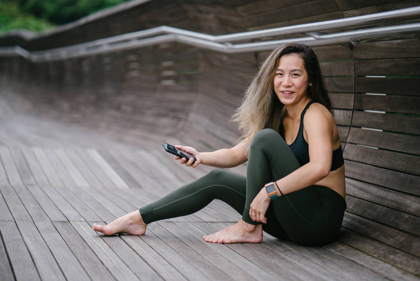 Portrait of an attractive, young Chinese Asian woman dressed in sporty, active wear with phone.  - Фото, зображення
