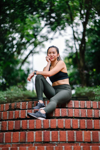 Portrait of an attractive, young Chinese Asian woman dressed in sporty, active wear on a bridge in a lush, green public park in Singapore during the day on the weekend. - Zdjęcie, obraz