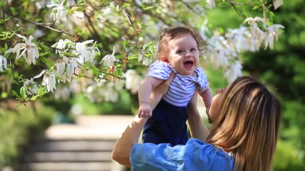 Jonge roodharige moeder en kind hebben een vrijetijdsbesteding in lente magnolia bloeiende tuin op zonnige dag - Video