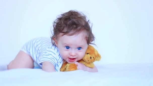 Little child boy with blue eyes and teddy bear in white bed - Felvétel, videó