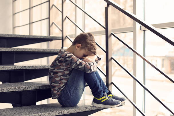 Depressed little boy sitting on stairs indoors. Time to visit child psychologist - Foto, imagen