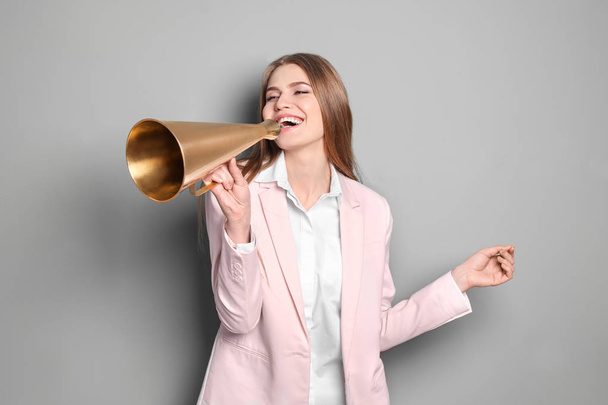Young woman using megaphone on grey background - Foto, afbeelding