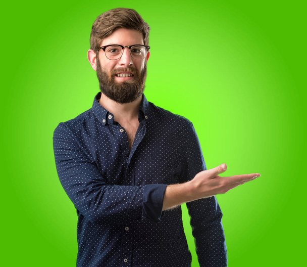 Giovane hipster uomo con grande barba che tiene qualcosa nella sua mano vuota su sfondo verde
 - Foto, immagini
