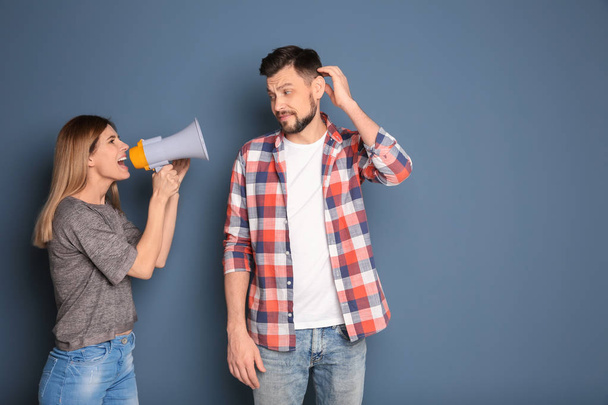 Young woman with megaphone shouting at man on color background - Foto, Imagen