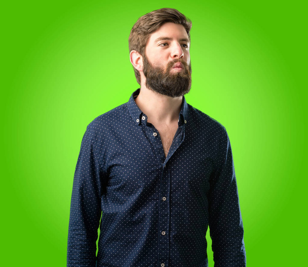 Young hipster man with big beard expressing love, blows kiss at camera, flirting over green background - Photo, Image