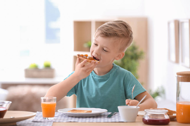 Cute little boy eating tasty toasted bread with jam at table - Foto, immagini