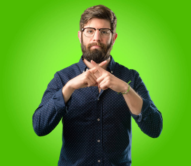 Young hipster man with big beard annoyed with bad attitude making stop sign with hand, saying no, expressing security, defense or restriction, maybe pushing over green background - Fotó, kép