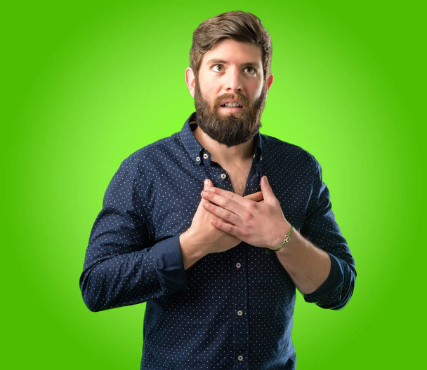 Jeune homme hipster avec une grosse barbe ayant un sourire charmant tenant la main sur le cœur voulant montrer de l'amour et de la sympathie sur fond vert
 - Photo, image