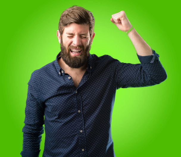 junger Hipster-Mann mit dickem Bart glücklich und aufgeregt mit Siegergeste. erfolgreich und siegreich, triumphierend über grünen Hintergrund - Foto, Bild