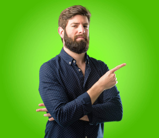 緑の背景の上の指離れ側を指す大きなひげを持つ若いヒップな男 - 写真・画像