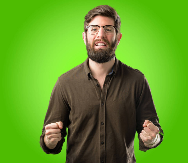 Young hipster man with big beard happy and excited celebrating victory expressing big success, power, energy and positive emotions. Celebrates new job joyful over green background - Photo, Image