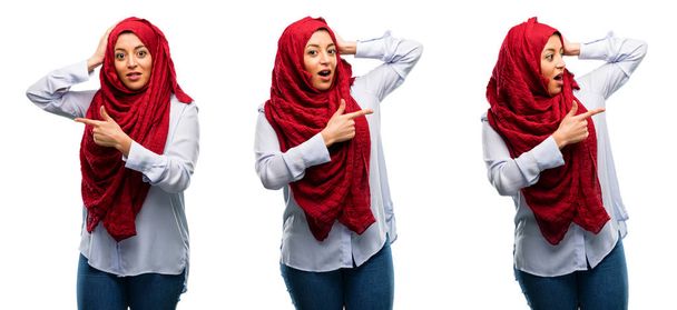 arabische Frau trägt Hijab und zeigt mit dem Finger zur Seite über weißem Hintergrund - Foto, Bild
