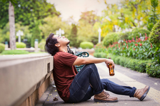 Triste único asiático homem bebendo cerveja e sentado no chão no parque público
. - Foto, Imagem