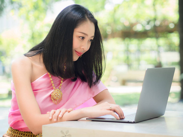 Thai woman in traditional costume is using a laptop in the garde - Foto, Bild