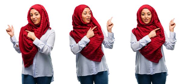 Mujer árabe con hiyab apuntando hacia un lado con el dedo aislado sobre fondo blanco
 - Foto, imagen