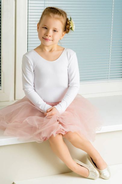 A little girl is sitting by the window with jalousie - Zdjęcie, obraz