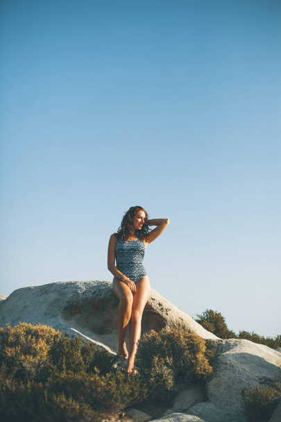 Csinos, fiatal nő ül a tenger sziklás partján egy napsütéses nyári nap - Fotó, kép