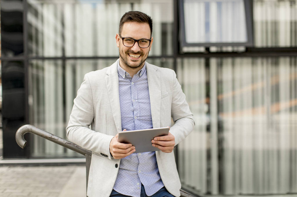 Handsome young businessman with digital tablet by the office building - Fotografie, Obrázek