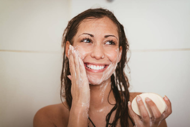 νέοι χαμογελαστό γυναίκα πρόσωπο πλύσιμο με σαπούνι στο μπάνιο - Φωτογραφία, εικόνα