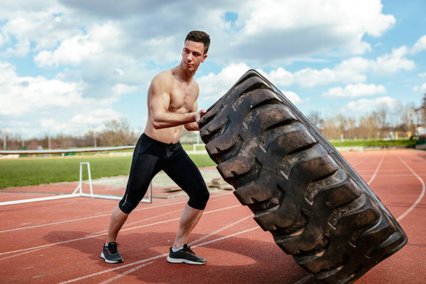 Hombre musculoso joven levantando neumático enorme para los músculos de entrenamiento en el estadio
 - Foto, imagen