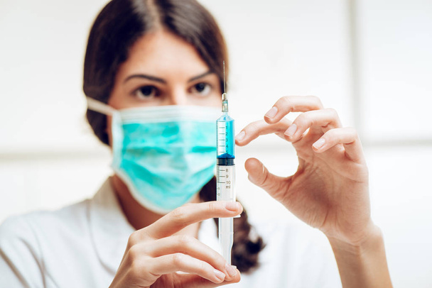 Молодая медсестра в маске готовит инъекцию анестезии
 - Фото, изображение