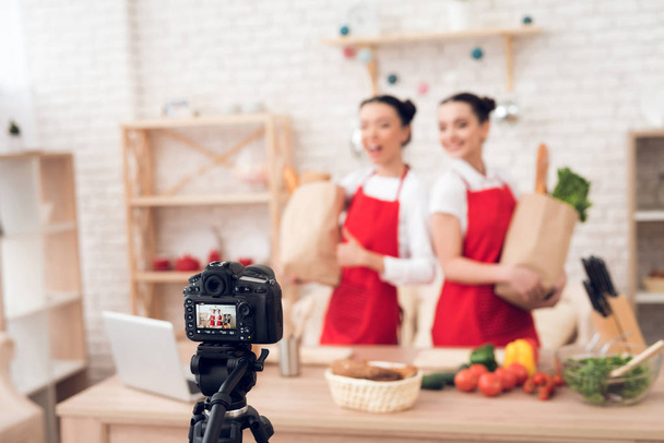 Two culinary bloggers in red aprons holding packages with food to camera - Fotografie, Obrázek