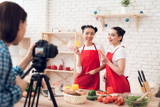 Two culinary bloggers in red aprons hold up diced peppers to camera. - Foto, Imagem