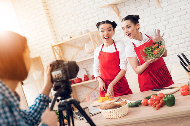 Two culinary bloggers in red aprons mixing diced peppers with salad to camera. - 写真・画像