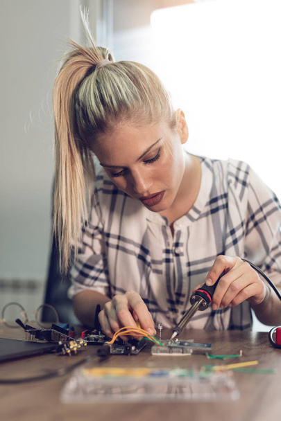 Young woman technician focused on repairing of electronic equipment by soldering iron - Foto, immagini