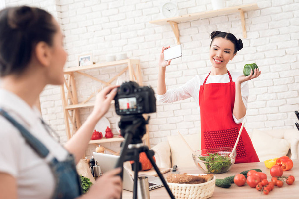 スマート フォン、カメラの後ろに一人の女の子に selfie を取って赤のエプロンで 2 つの料理ブロガー - 写真・画像