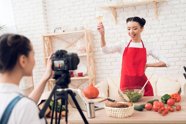 Two female culinary bloggers in red aprons tasting wine, one girl behind camera - Foto, Imagem