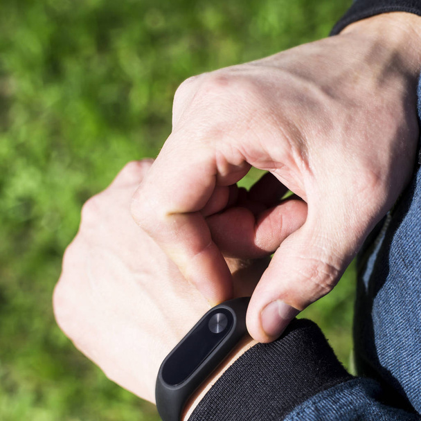 Фітнес-браслет або розумний годинник на руці чоловіка. На тлі зеленої трави. Дорослий чоловік у блакитній смузі. Концепція здорового способу життя
 - Фото, зображення