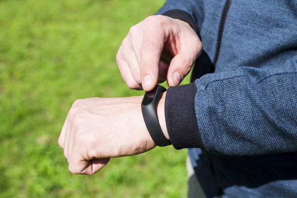 Bracelet de fitness ou montre intelligente sur la main d'un homme. Dans le contexte de l'herbe verte. Un mâle adulte dans une bande bleue. Concept de mode de vie sain
 - Photo, image