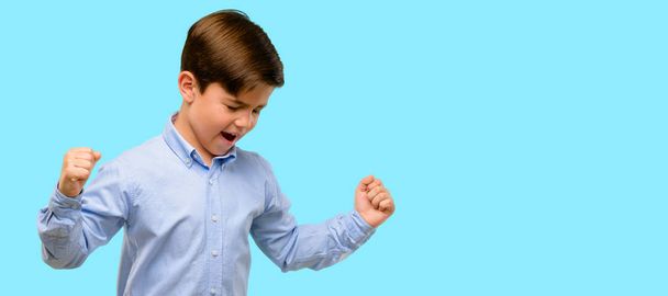 Pěkný batole dítě se zelenýma očima, šťastný a nadšený, vyjádření vítězné gesto. Úspěšné a slaví vítězství, vítězství nad modrým pozadím - Fotografie, Obrázek