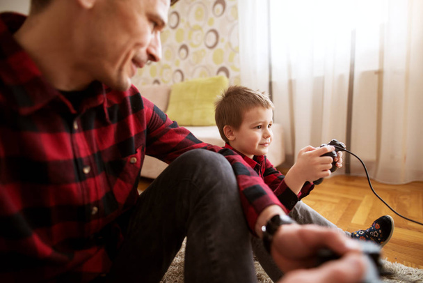 cheerful excited father and little son in red shirts playing console game with gamepads - Photo, Image
