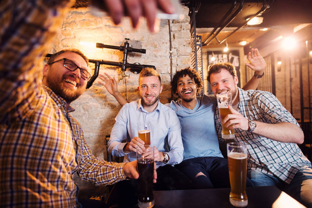 young happy bearded men drinking with beer in pub and taking selfie  - Photo, Image
